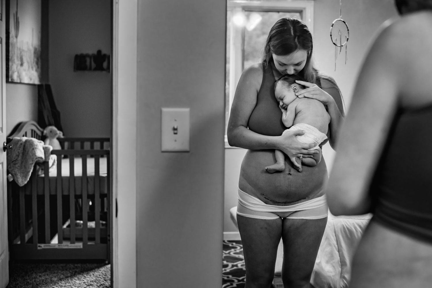 Person in white holding a newborn baby while standing in a dimly lit room.