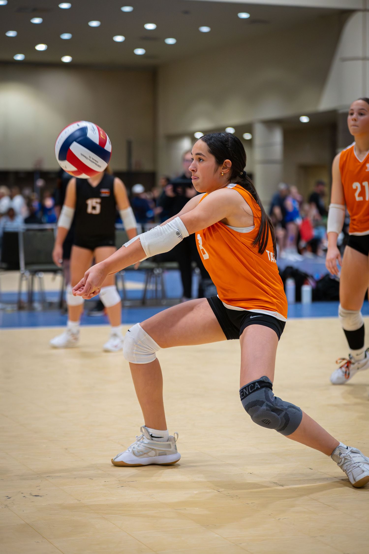 Female volleyball player #20 sets the ball during an indoor tournament match while teammate #33 prepares to spike.