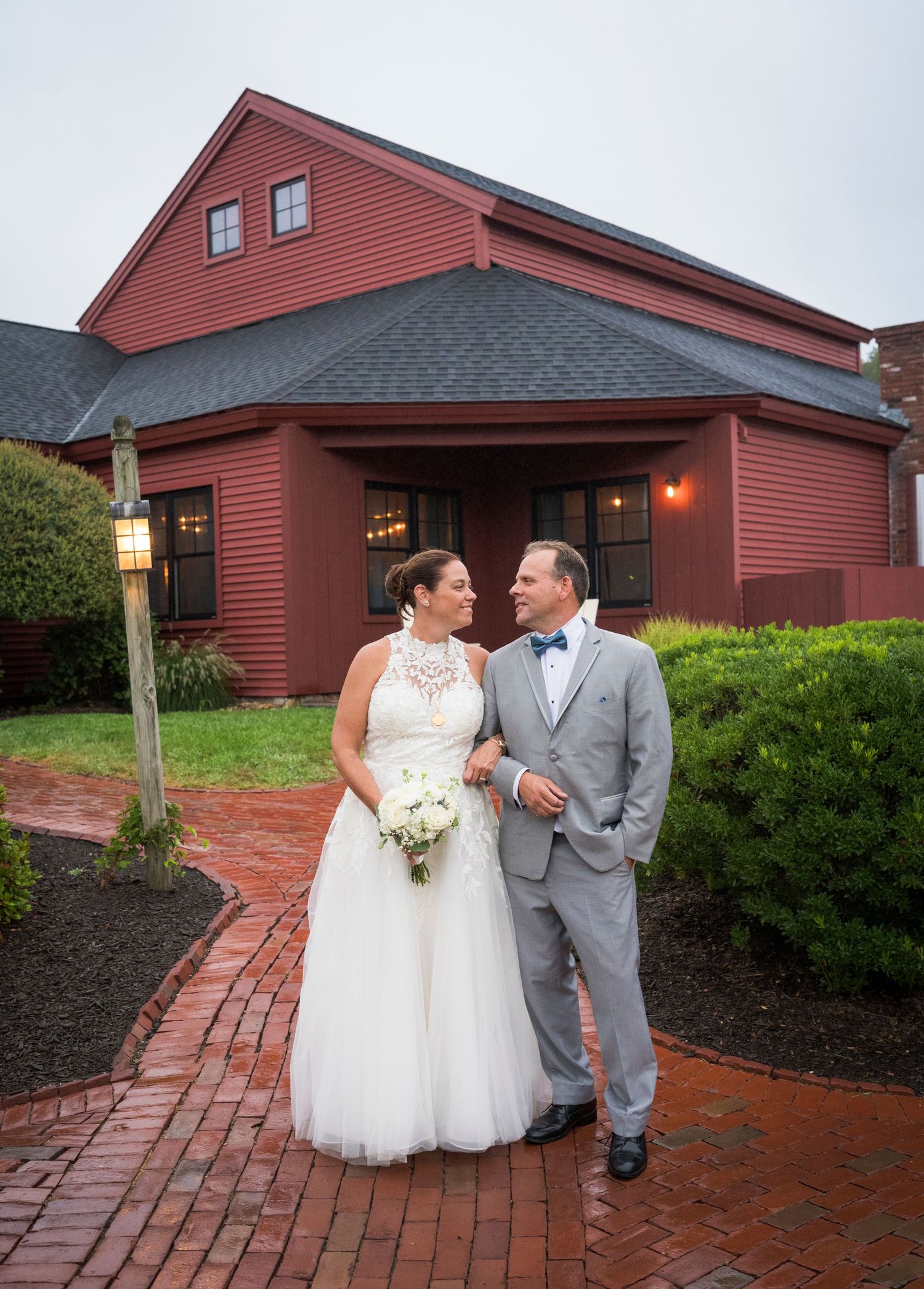 A winter wedding portrait outside a white farmhouse with illuminated windows and a full moon.