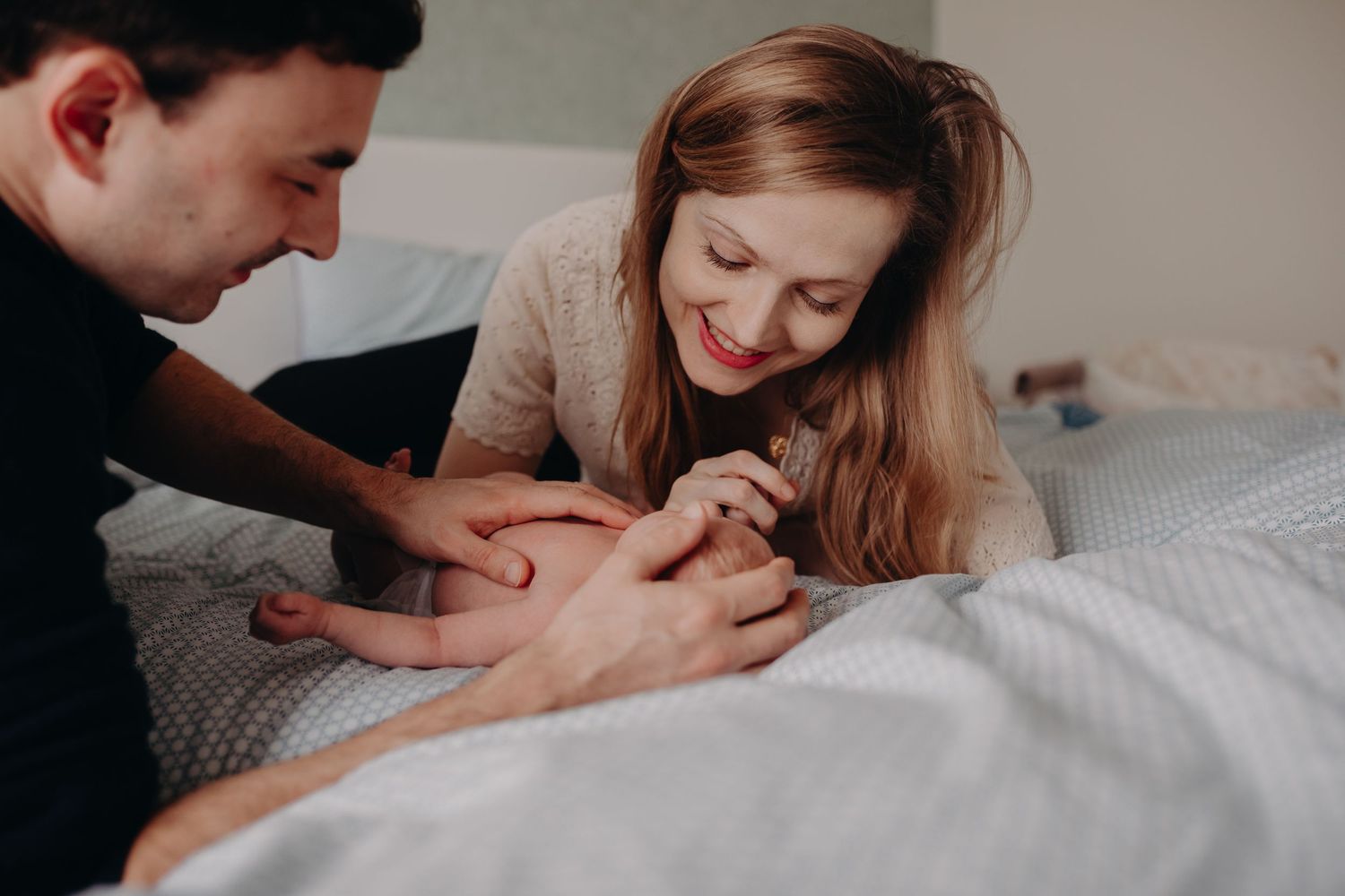 Smiling couple lying on a bed together admiring their newborn babys tiny feet.