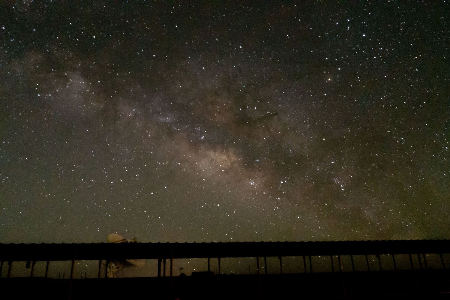Stunning Milky Way galaxy visible over a dark silhouetted building in a clear night sky full of stars.