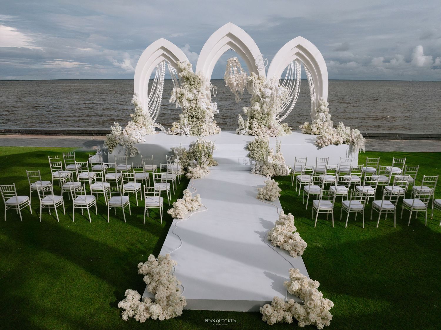 Elegant outdoor wedding ceremony setup with white floral arrangements, arch decor, and chairs overlooking a serene waterfront.