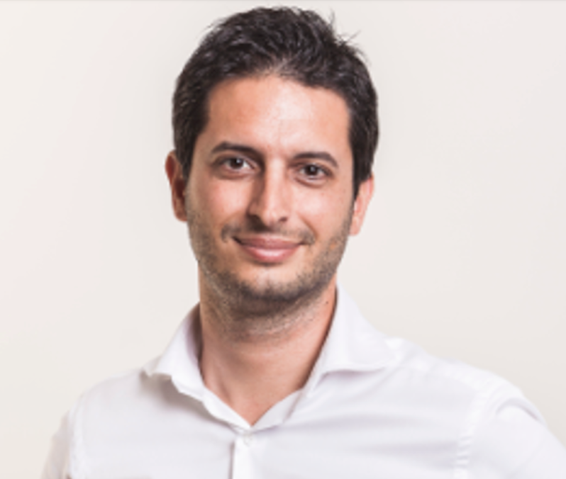 Professional headshot of someone in a white button-down shirt against a light background with a friendly expression.