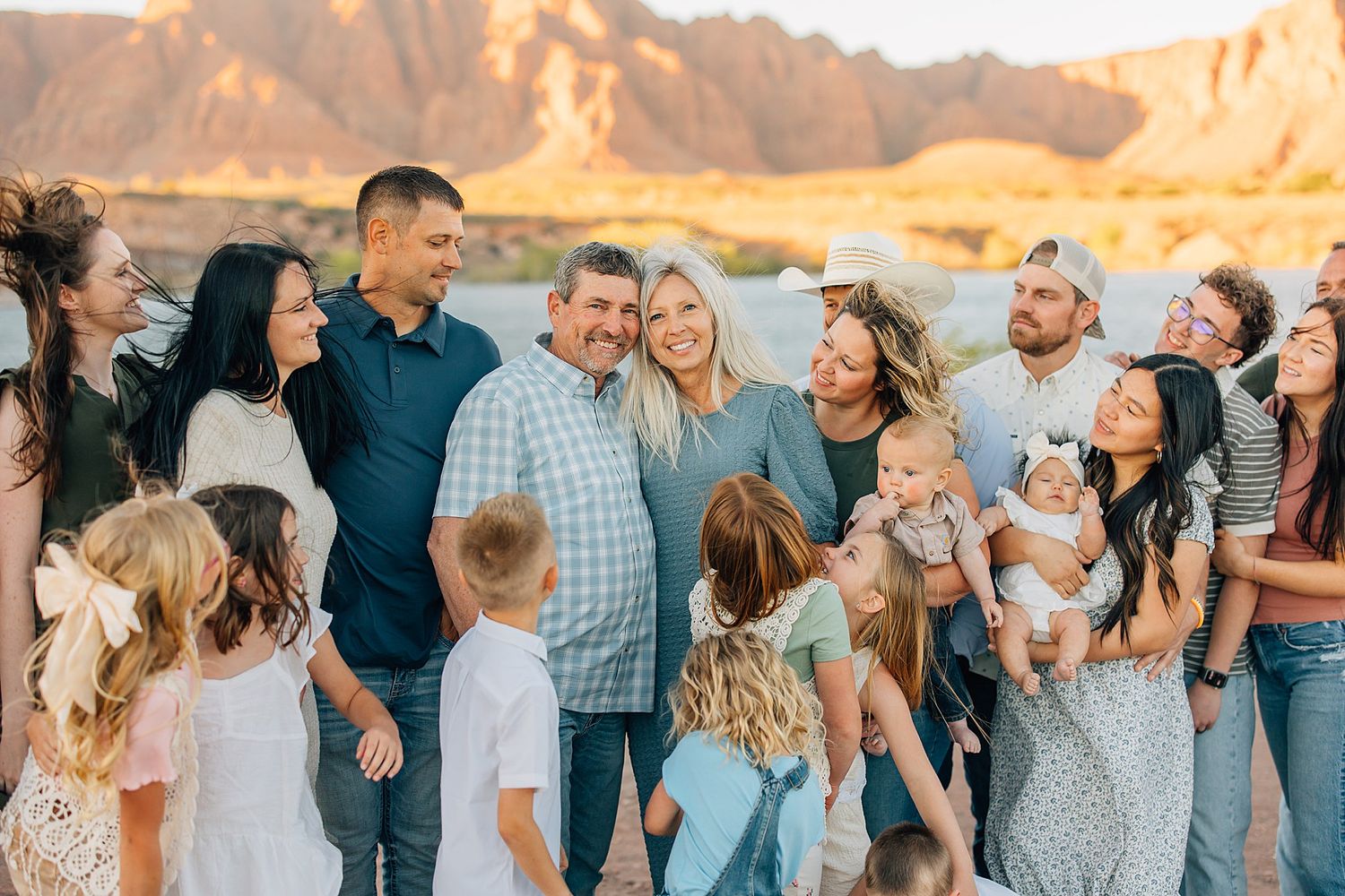 Large family group posing together outdoors near a river with red rock canyon cliffs glowing at sunset.