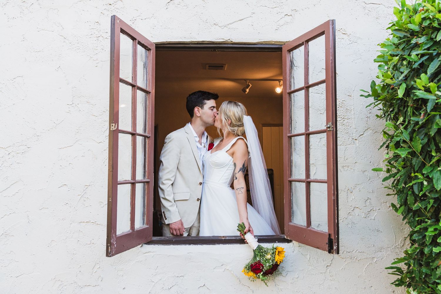 Romantic couple embraces by open window with white walls and natural light streaming in.