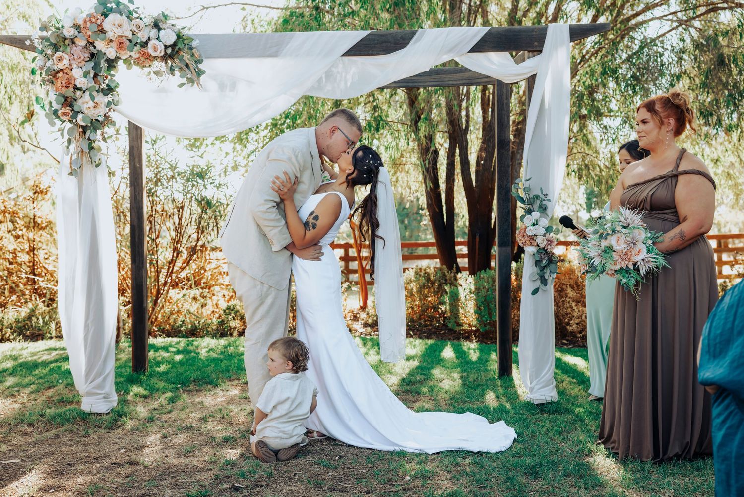 A romantic outdoor wedding ceremony under white drapes with floral arrangements in a garden setting.
