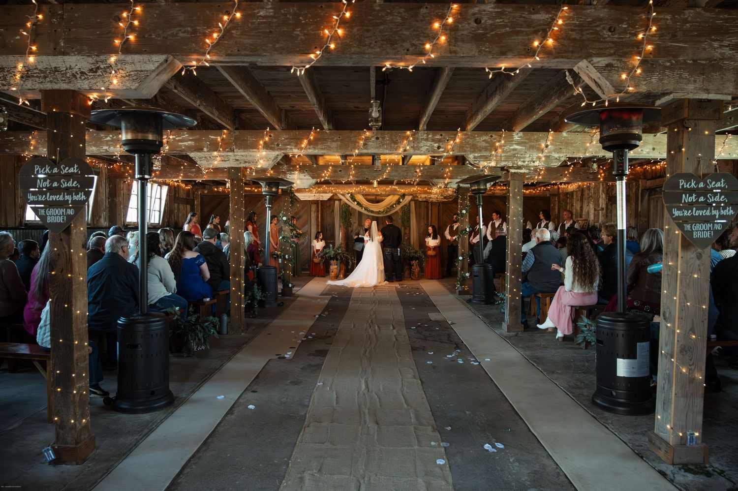 Rustic barn wedding venue with string lights creating a romantic aisle lined with guests.