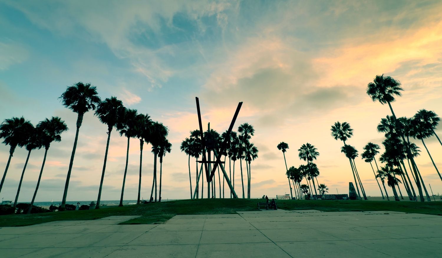 Silhouetted palm trees and abstract sculpture against a vibrant sunset sky at Venice Beach, California.