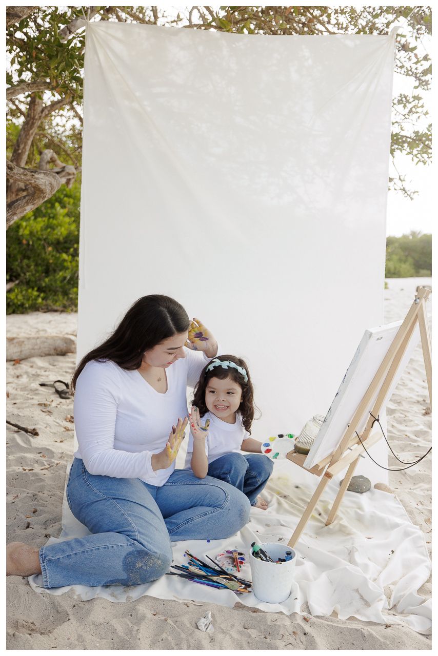 A family plays together on a beach, lifting a child in the air while wearing white clothing in black and white photography.