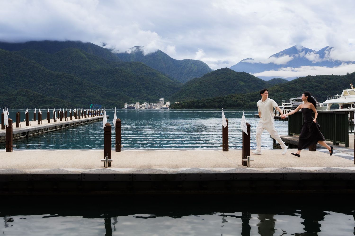 Couple posing on a dock at Sun Moon Lake, Taiwan, with lush mountains and turquoise water in the background.