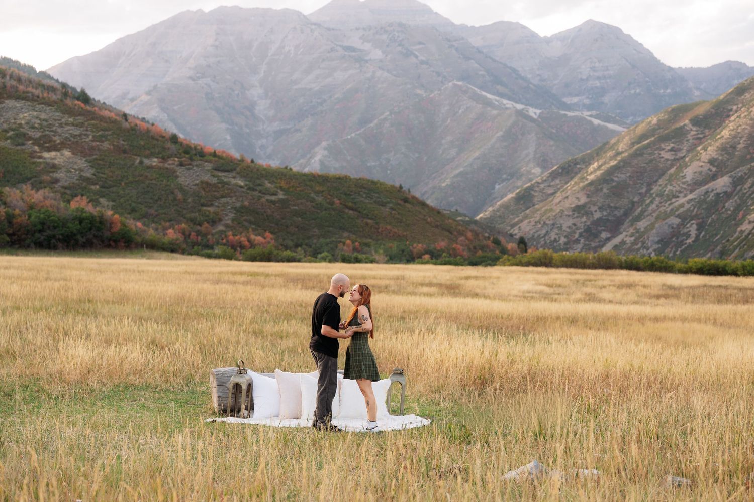 Couple sharing a romantic picnic in a golden field with dramatic mountain backdrop during autumn.