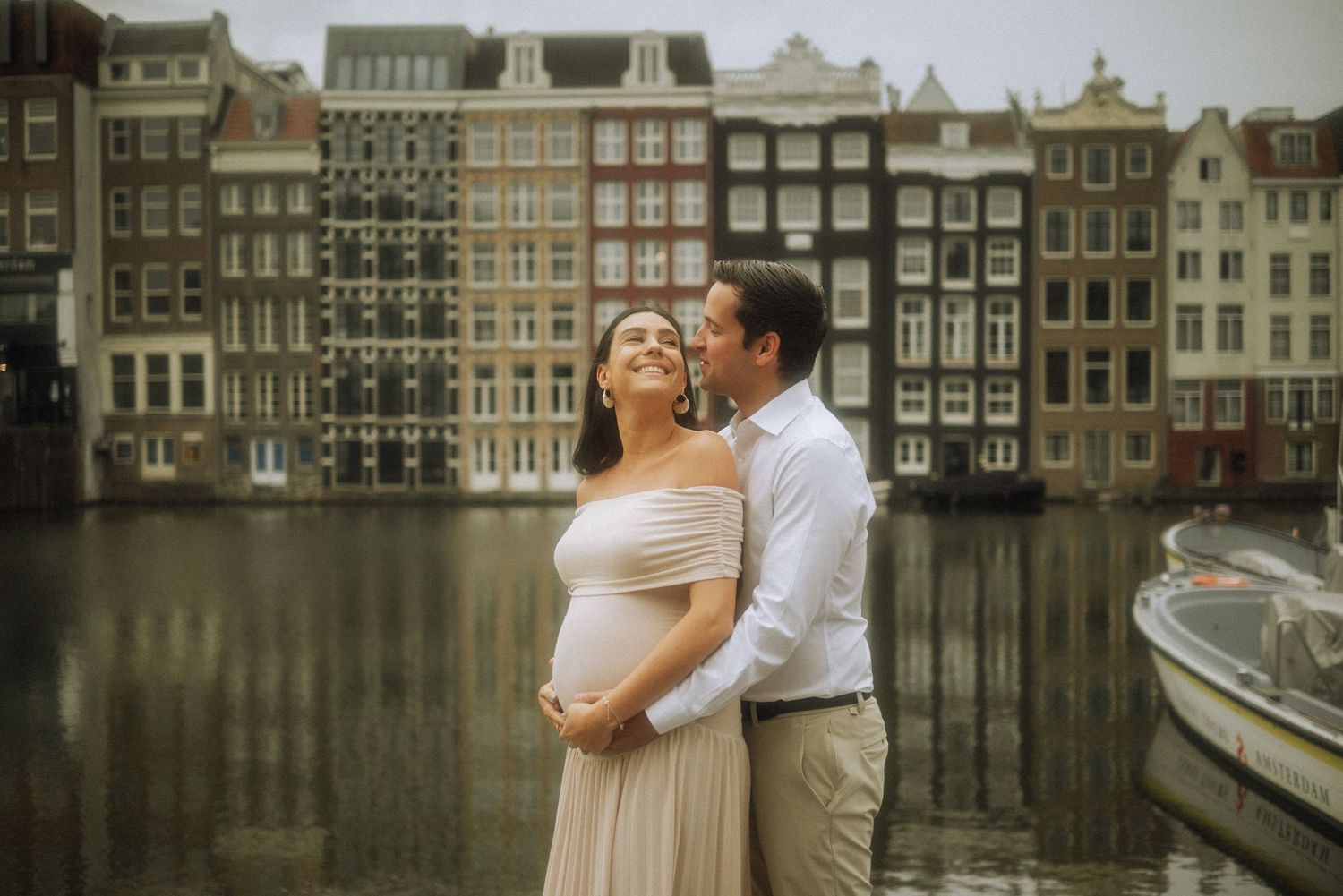 Pregnant couple in Amsterdam standing in front of the city’s iconic colorful canal houses