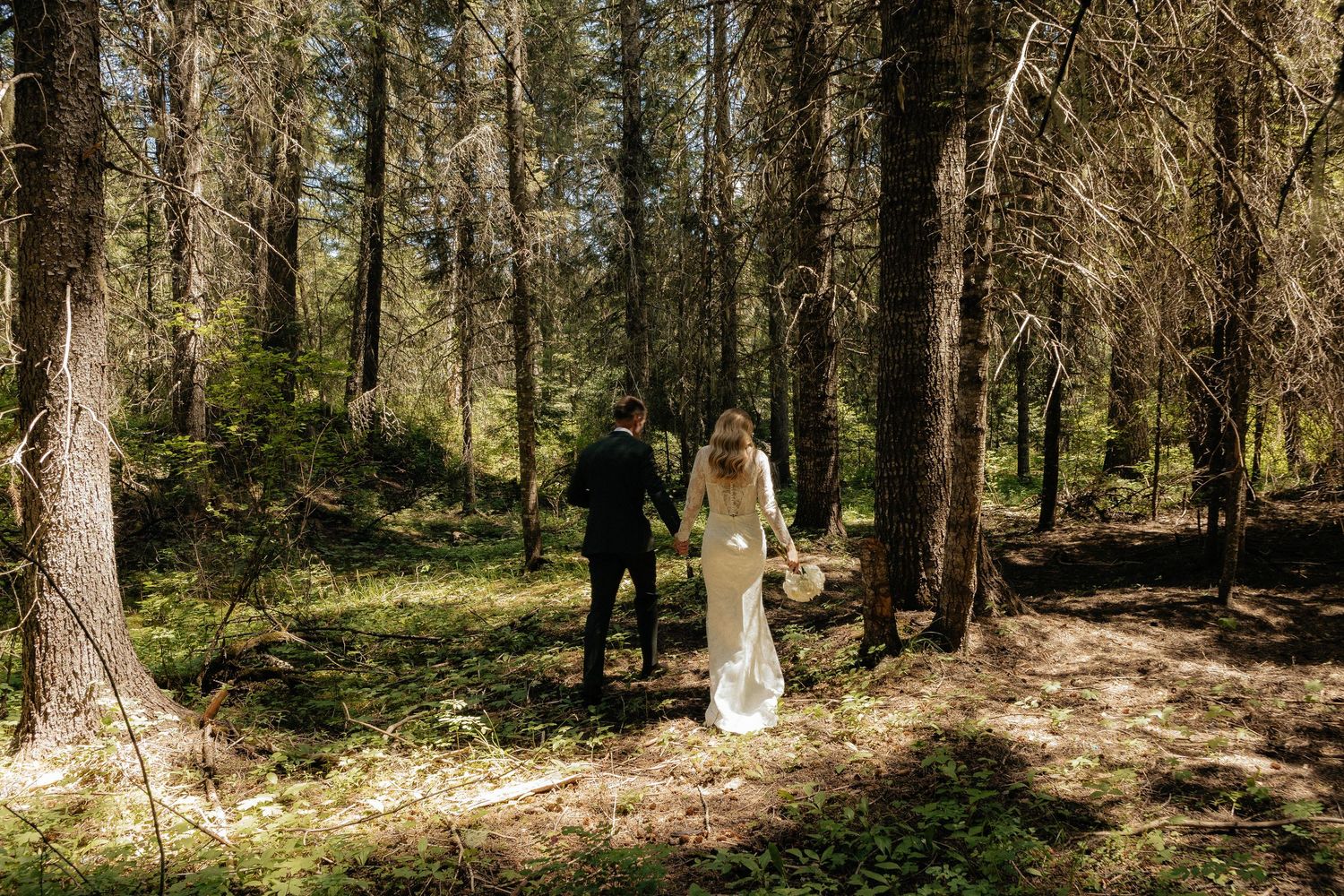 A couple having a romantic outdoor photo session in a sunlit forest wearing wedding attire.
