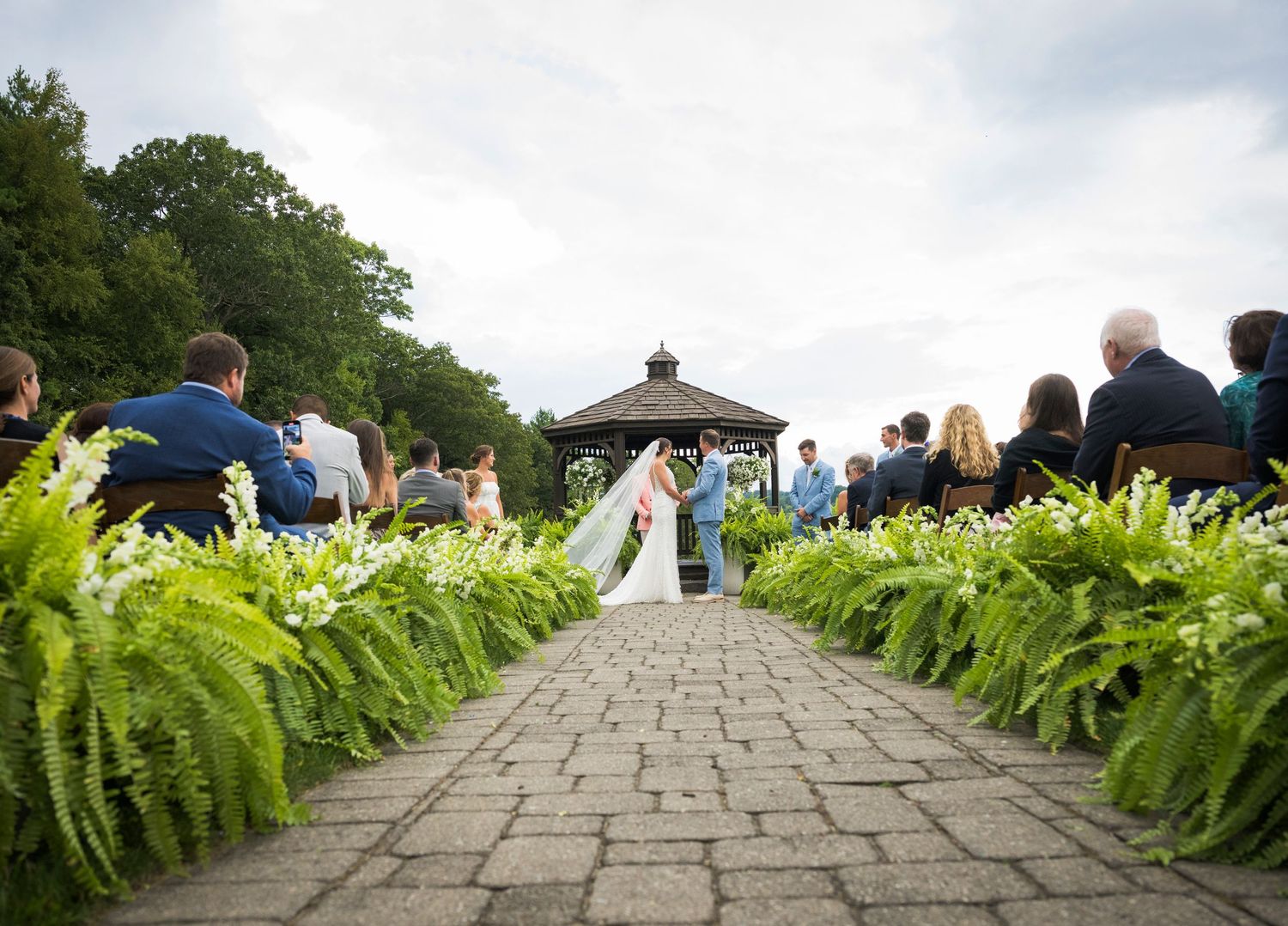 Newlyweds share an intimate moment outdoors with autumn foliage and rustic architecture in background.