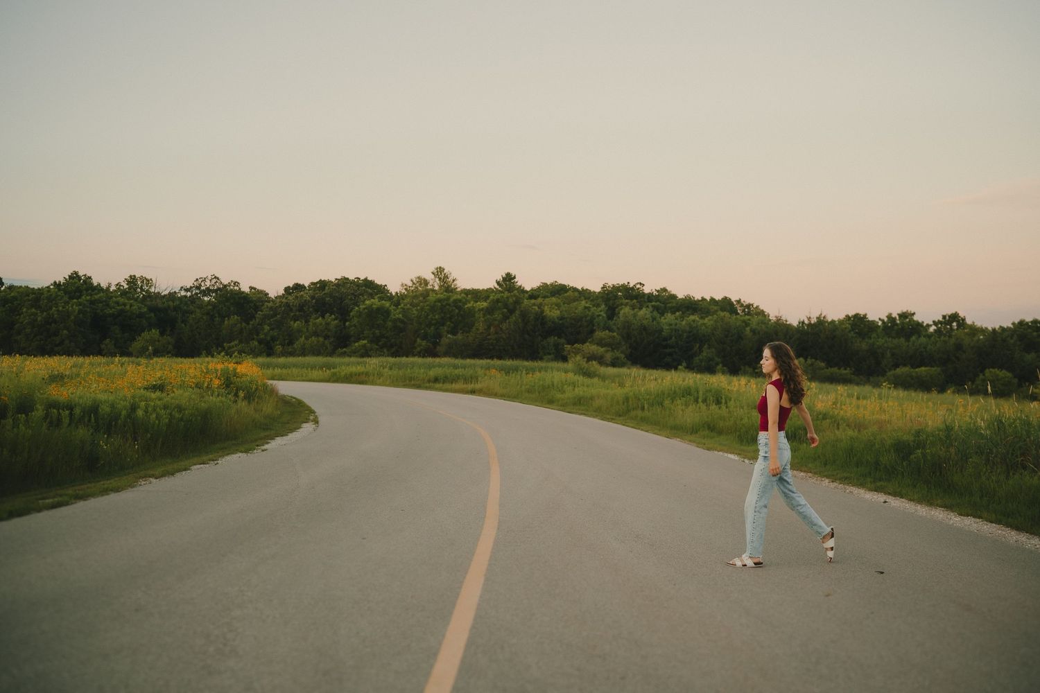 Solo jogger exercises on a curved rural road at sunset surrounded by green fields and trees.