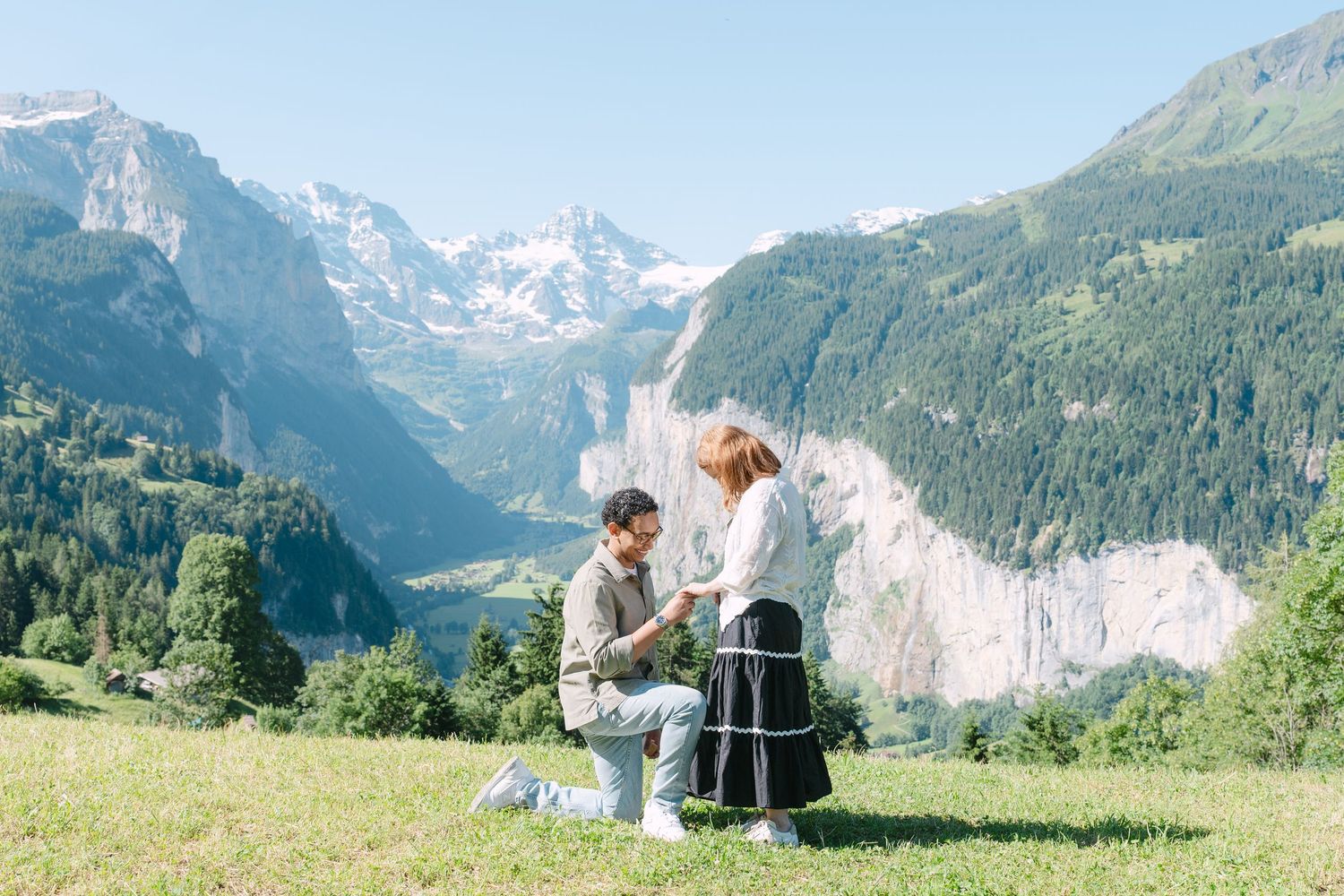 Two people hold hands on a grassy hill overlooking stunning Alpine mountains and valleys in Switzerland.