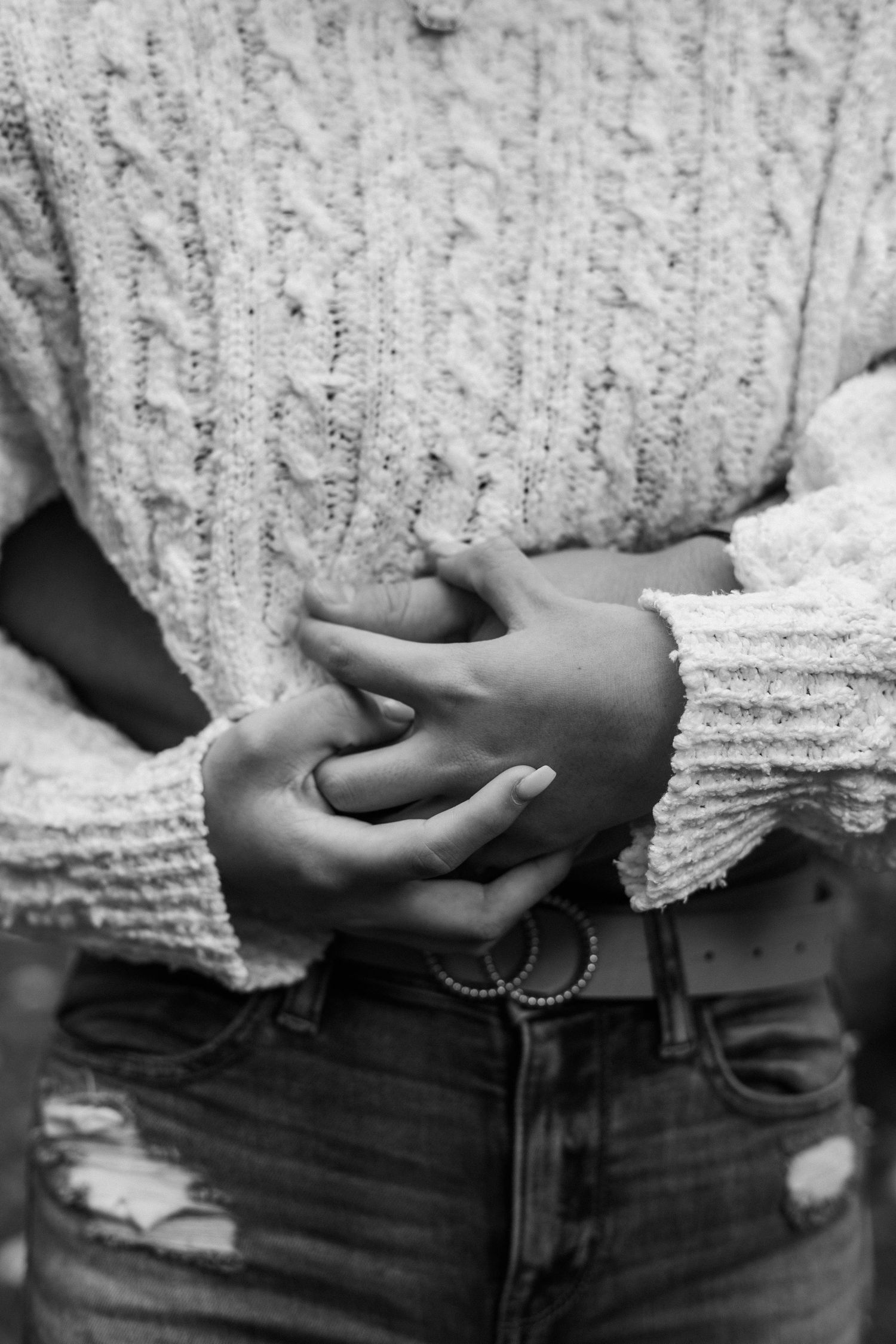 Close-up of hands clasped over cable knit sweater and distressed jeans in black and white.