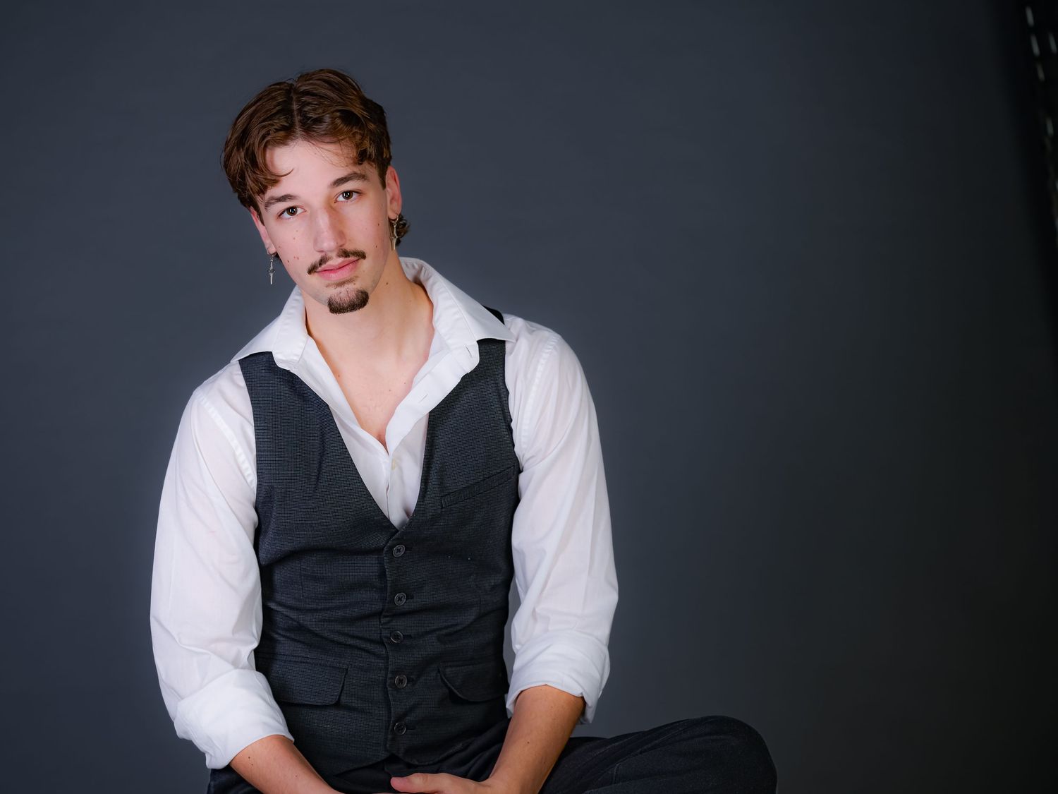 Studio portrait of someone wearing a black vest and white button-up shirt against a dark backdrop.