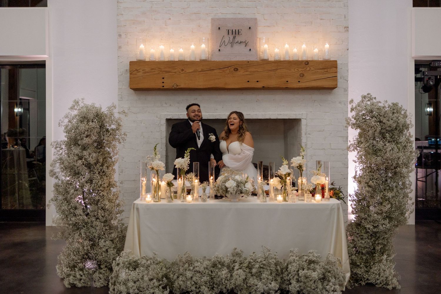 Elegant wedding reception table display with candles and floral arrangements in front of a white brick fireplace.
