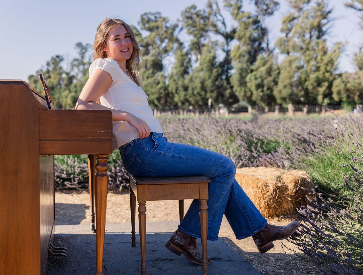 Person in casual attire sitting on wooden piano bench outdoors.
