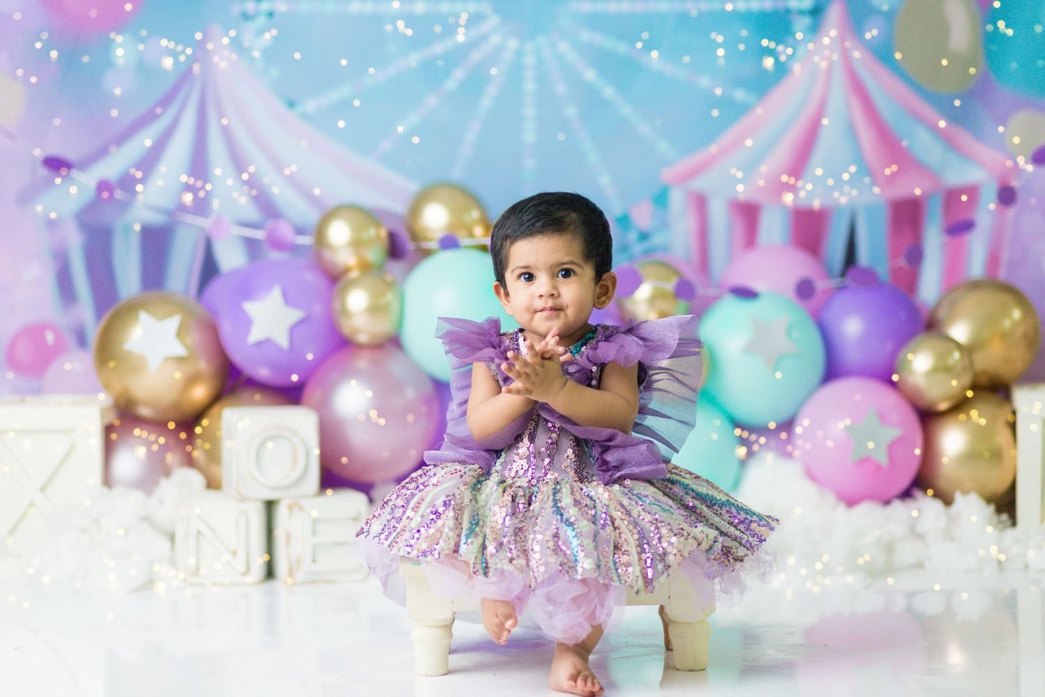 Purple and gold carnival themed photoshoot with balloons and circus tent backdrop.