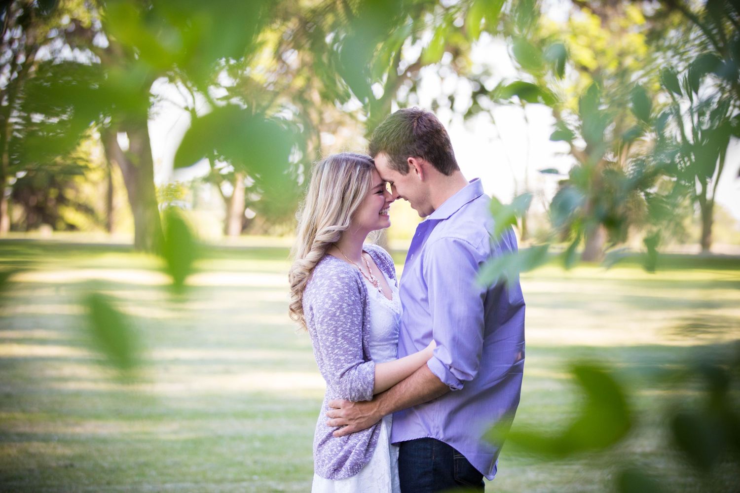 A romantic couple embraces in a sun-drenched park setting with soft bokeh effects.