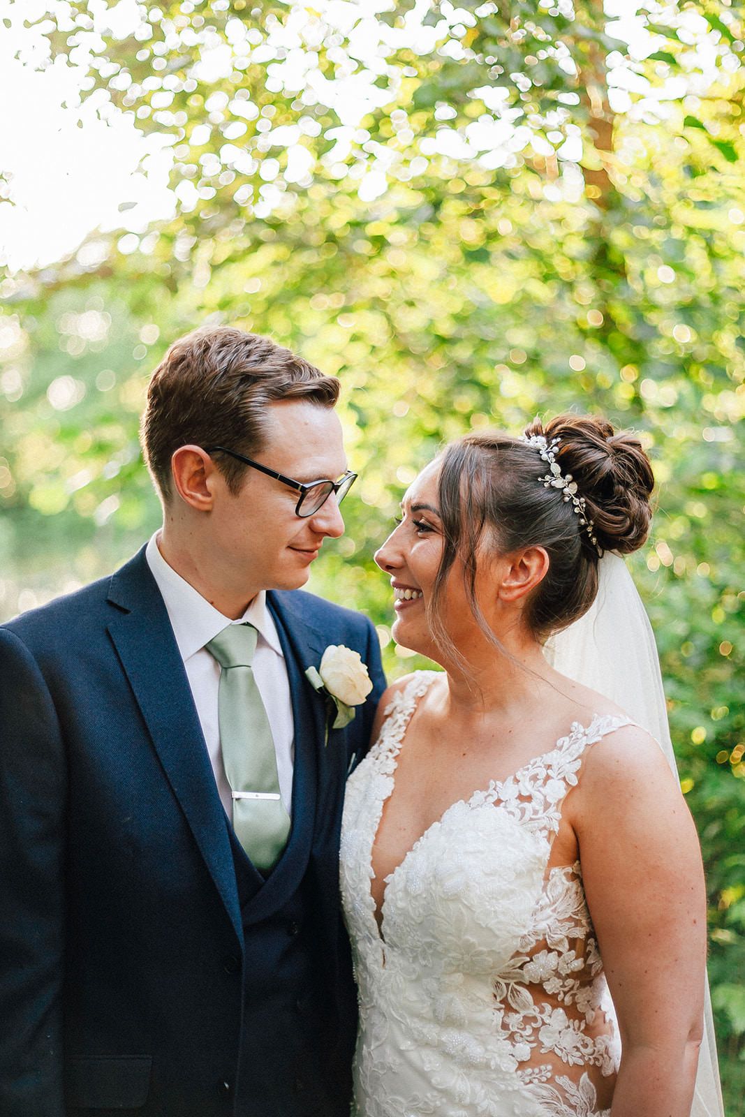 A joyful wedding couple share a tender moment outdoors against blurred green foliage.