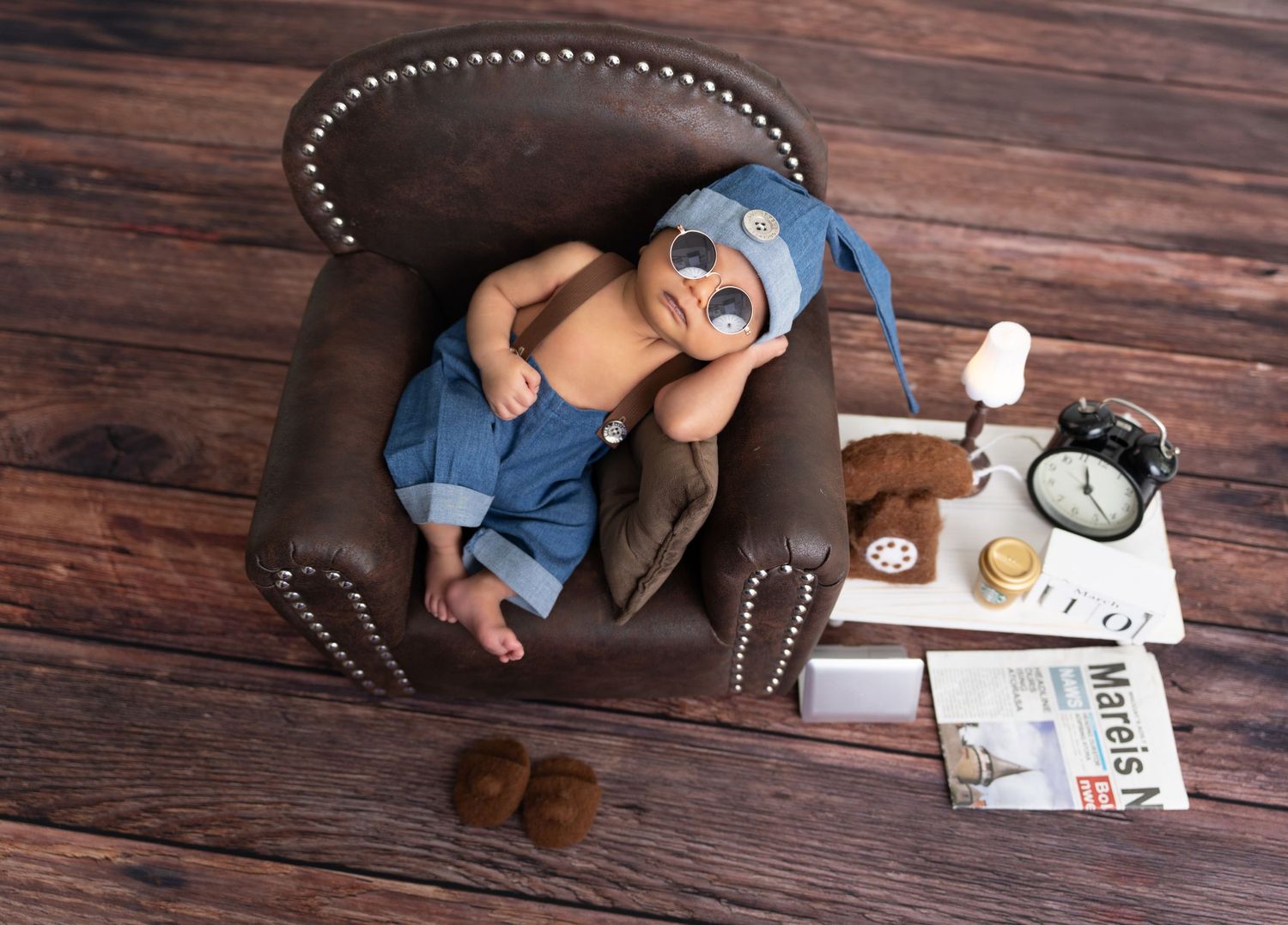 A tiny sleeper in blue rests on a brown leather armchair next to a side table with milk and an alarm clock.