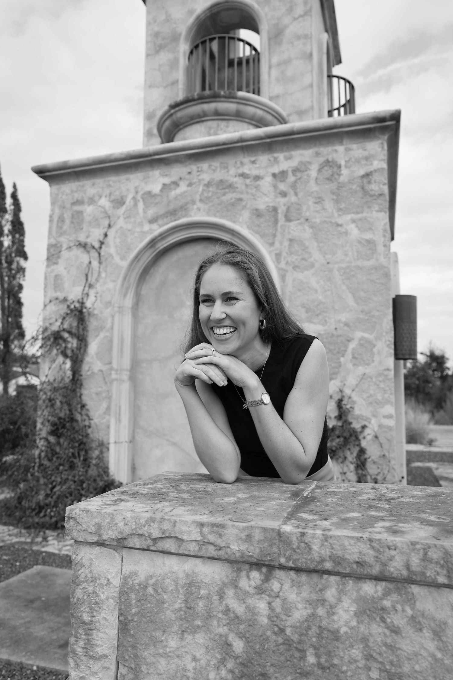 Black and white portrait of person leaning on stone wall with architectural details in background.