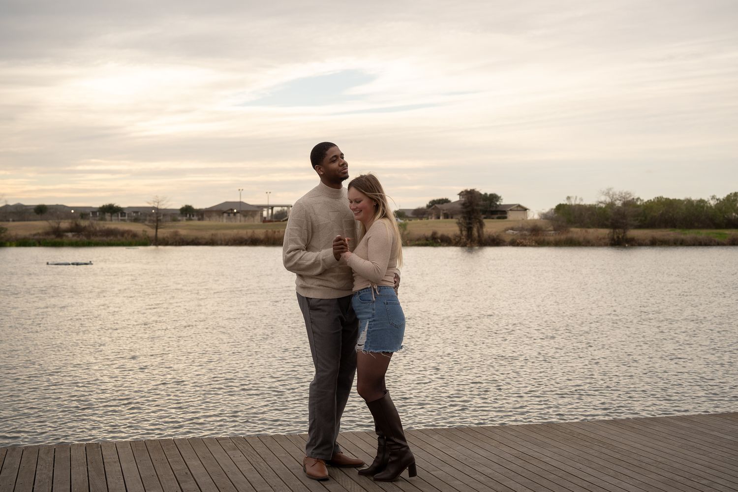 A couple shares an intimate moment on a lakeside dock at dusk.