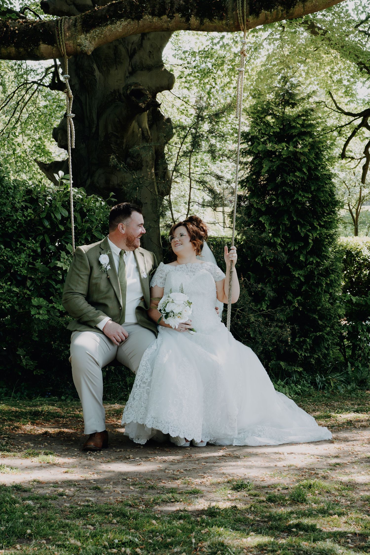 A couple shares a sweet moment on a rustic garden swing under a lush green arbor during their wedding celebration.