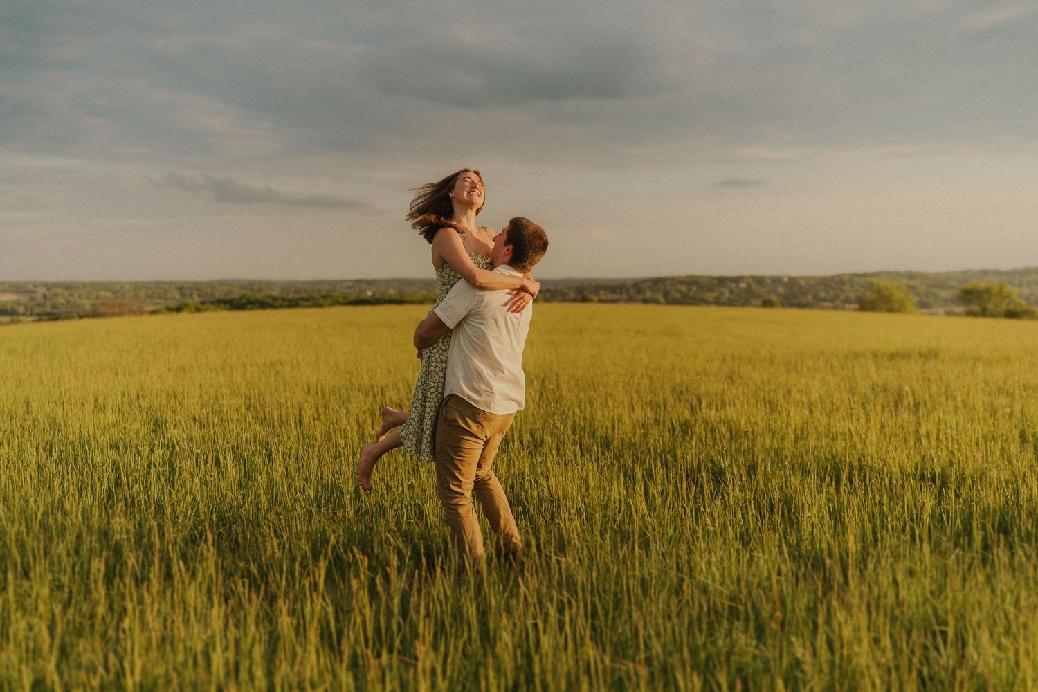 A couple embraces romantically in a golden wheat field at sunset.