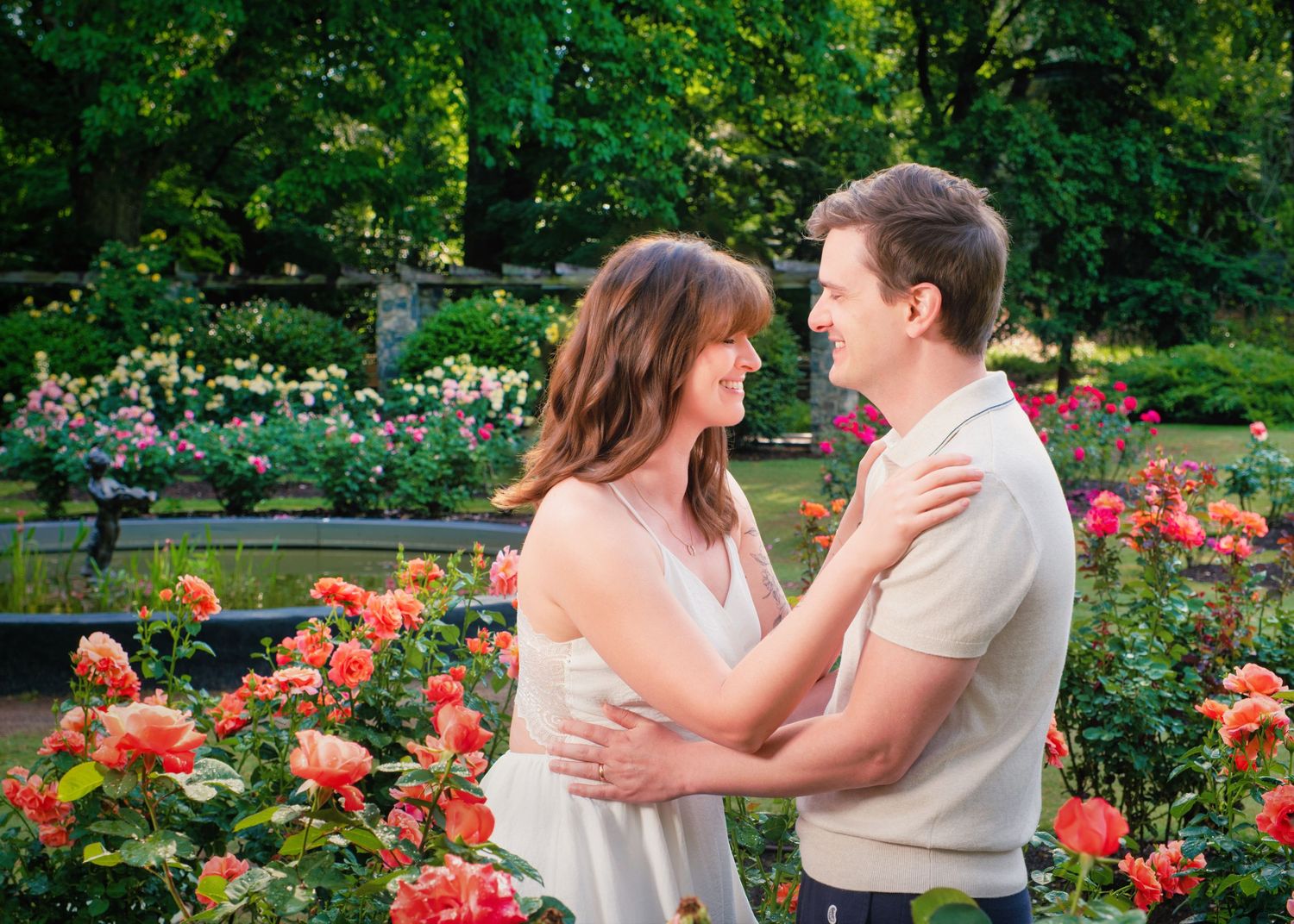 A couple embraces in a beautiful garden setting surrounded by blooming pink roses and lush greenery on a sunny day.