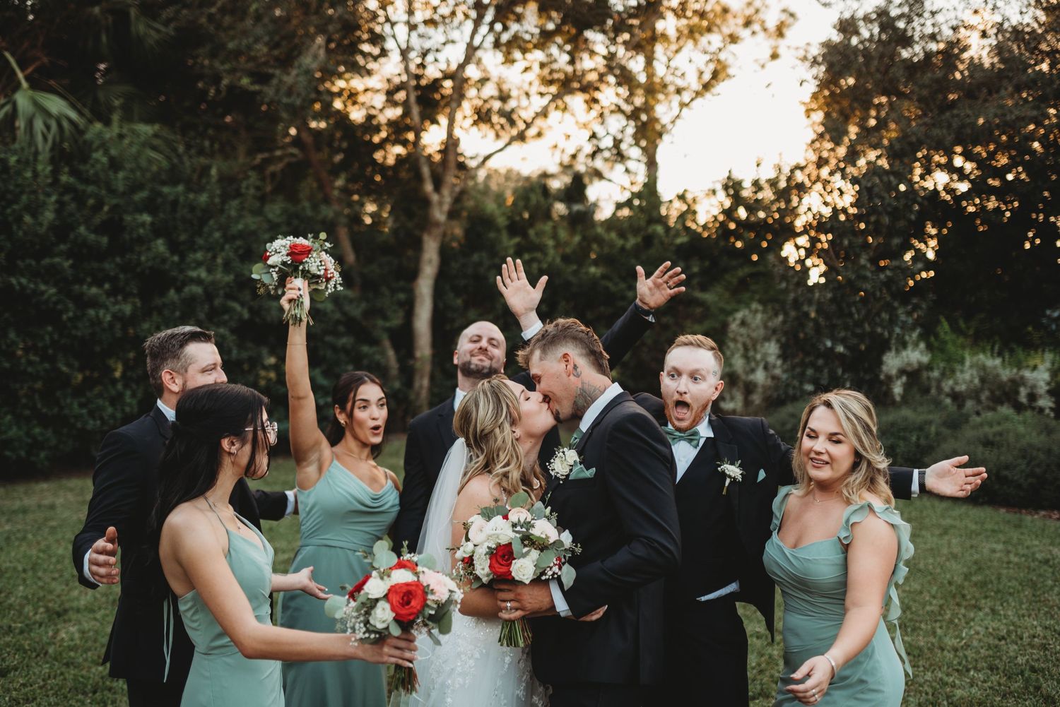 Wedding party celebrates joyfully on outdoor lawn at sunset.