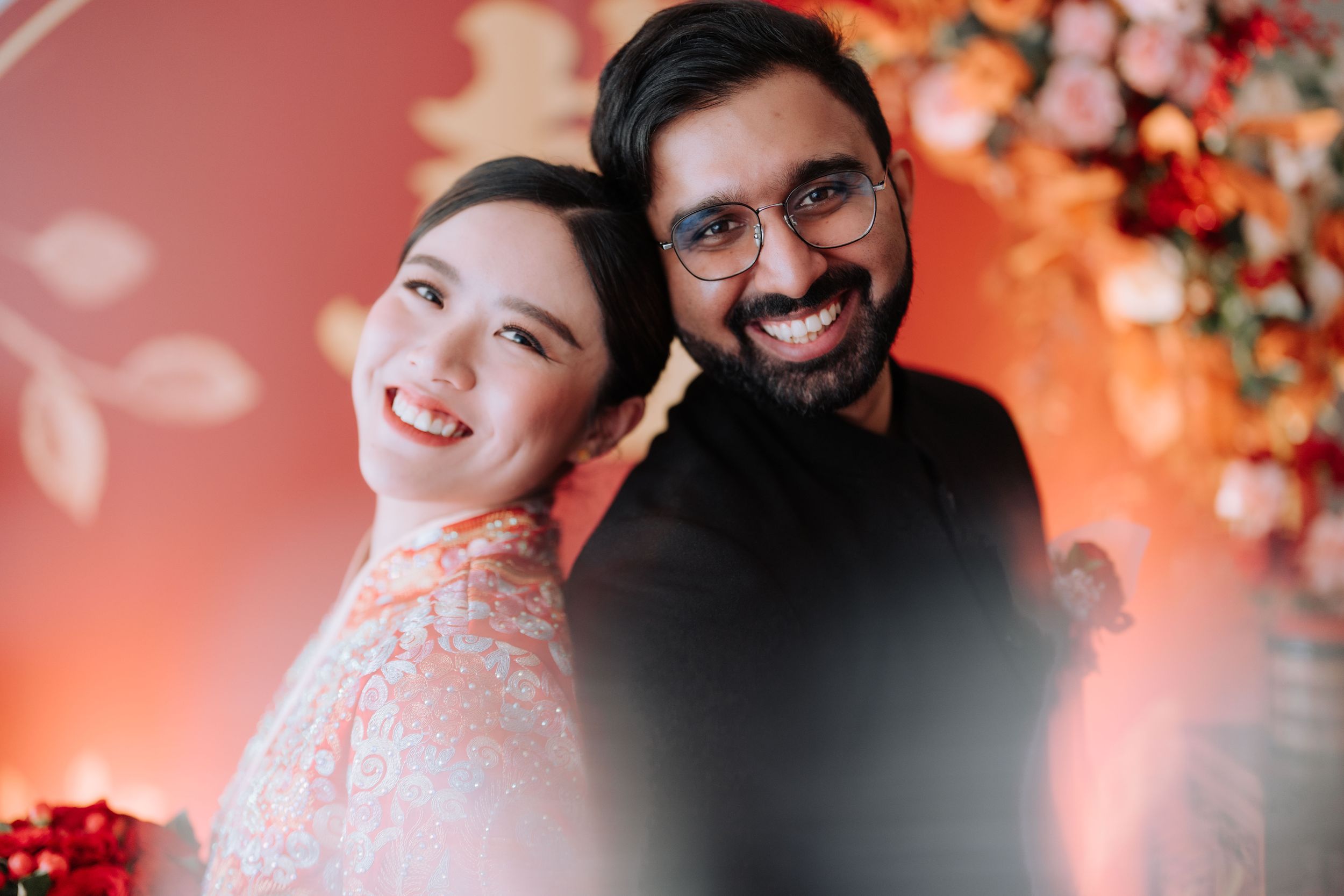A joyful couple smiles together in an engagement photo against a warm orange floral backdrop.