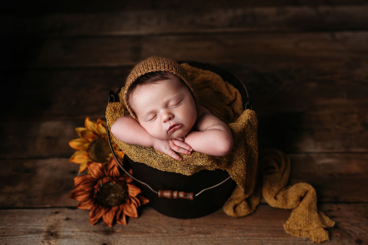 Autumn-themed newborn photography setup with sunflowers and wooden backdrop.