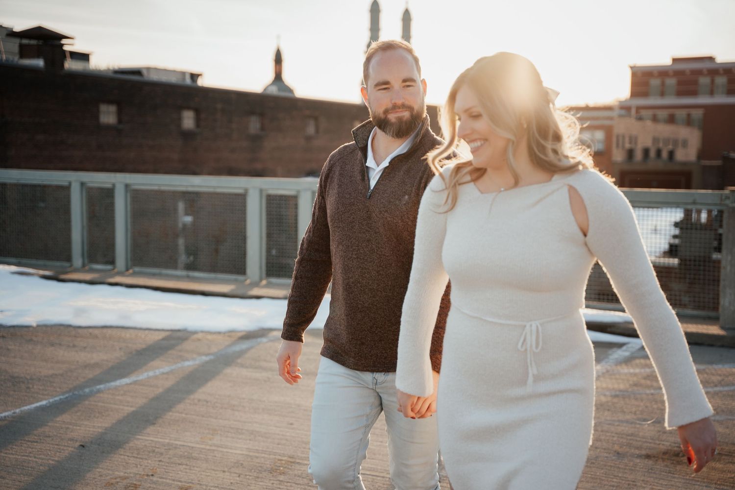 A couple walks together on a rooftop during golden hour in an urban setting.