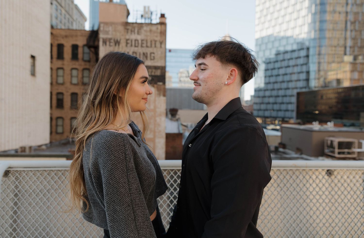 Two people share an intimate moment on an urban rooftop with city buildings in the background.