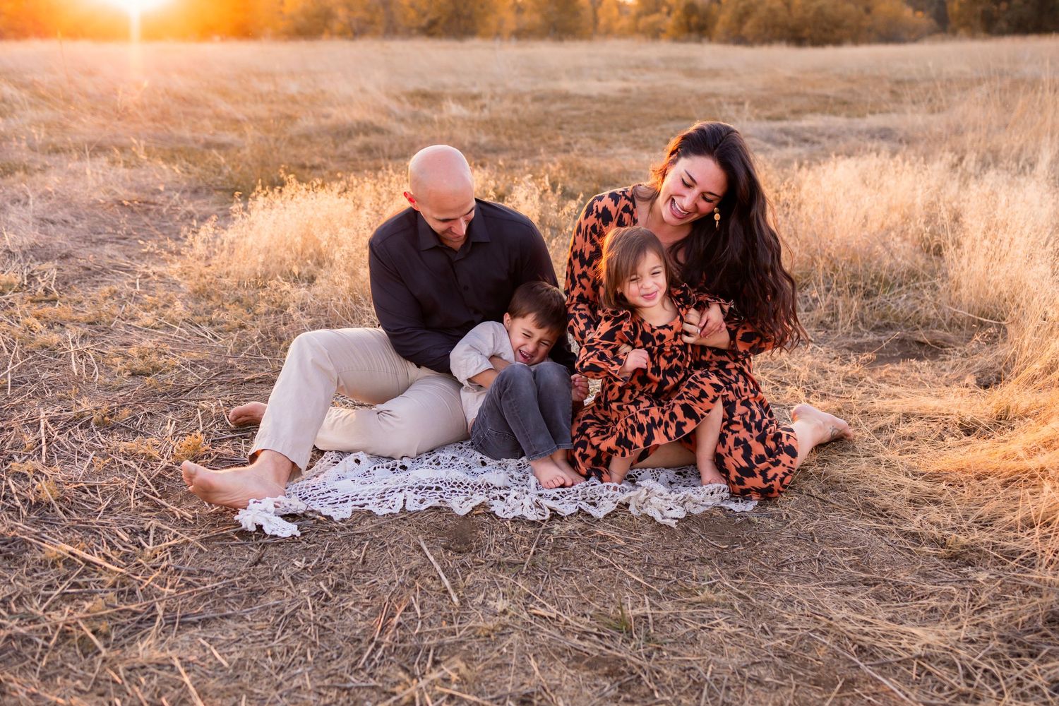 fall photoshoot, golden hour, family of four sat down outside, laughing and playing, mom, dad, little girl and boy