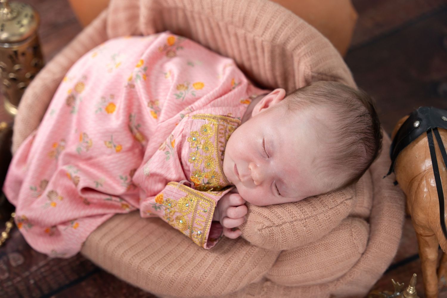 A sleeping baby wearing pink pajamas rests peacefully on a beige cushion.