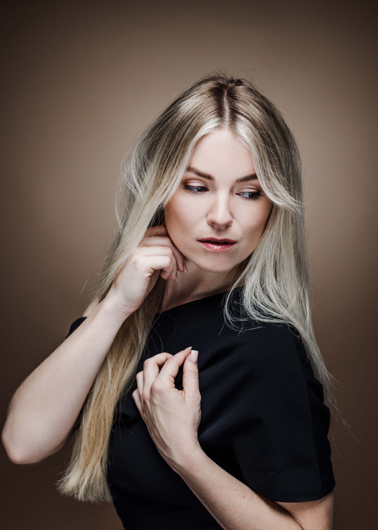 Portrait of a person with long blonde hair wearing a black top against a brown background in moody lighting.