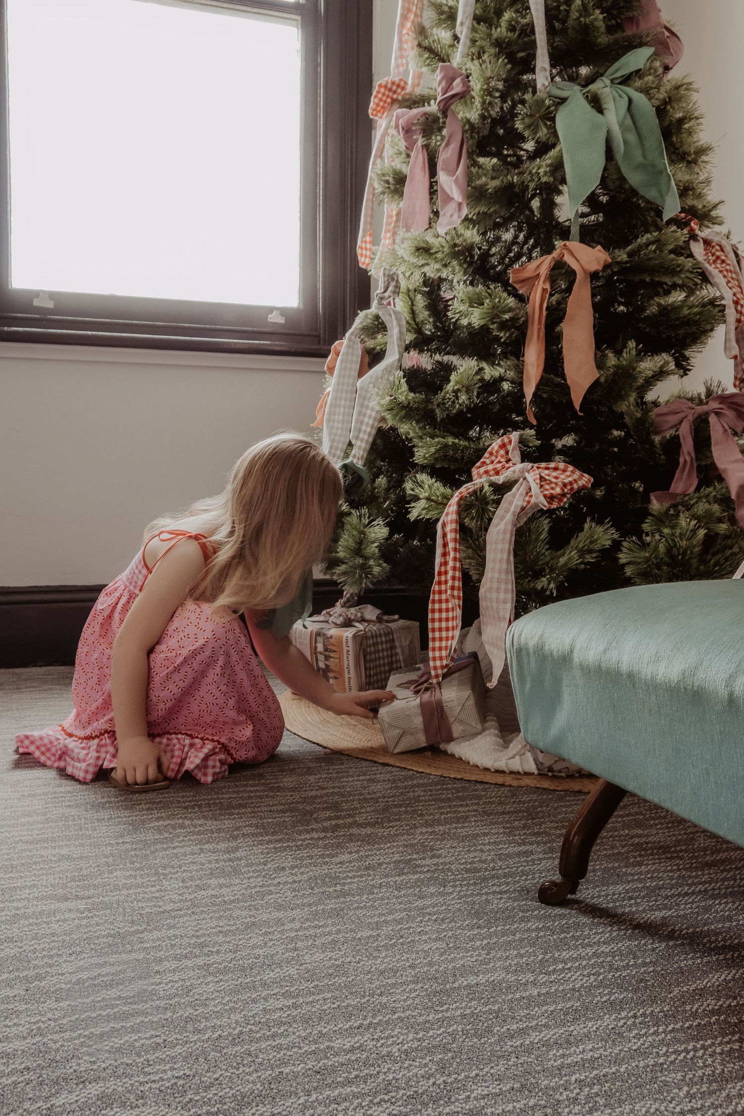 Little girl in a pink dresses sit and looks at christmas presents near a decorated Christmas tree at a Hunter Valley Christmas Session.