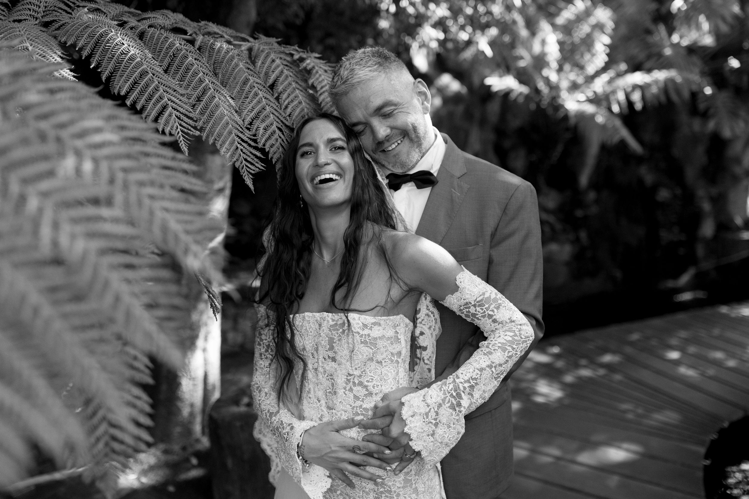 Black and white wedding photo showing a joyful couple laughing together during an outdoor celebration.