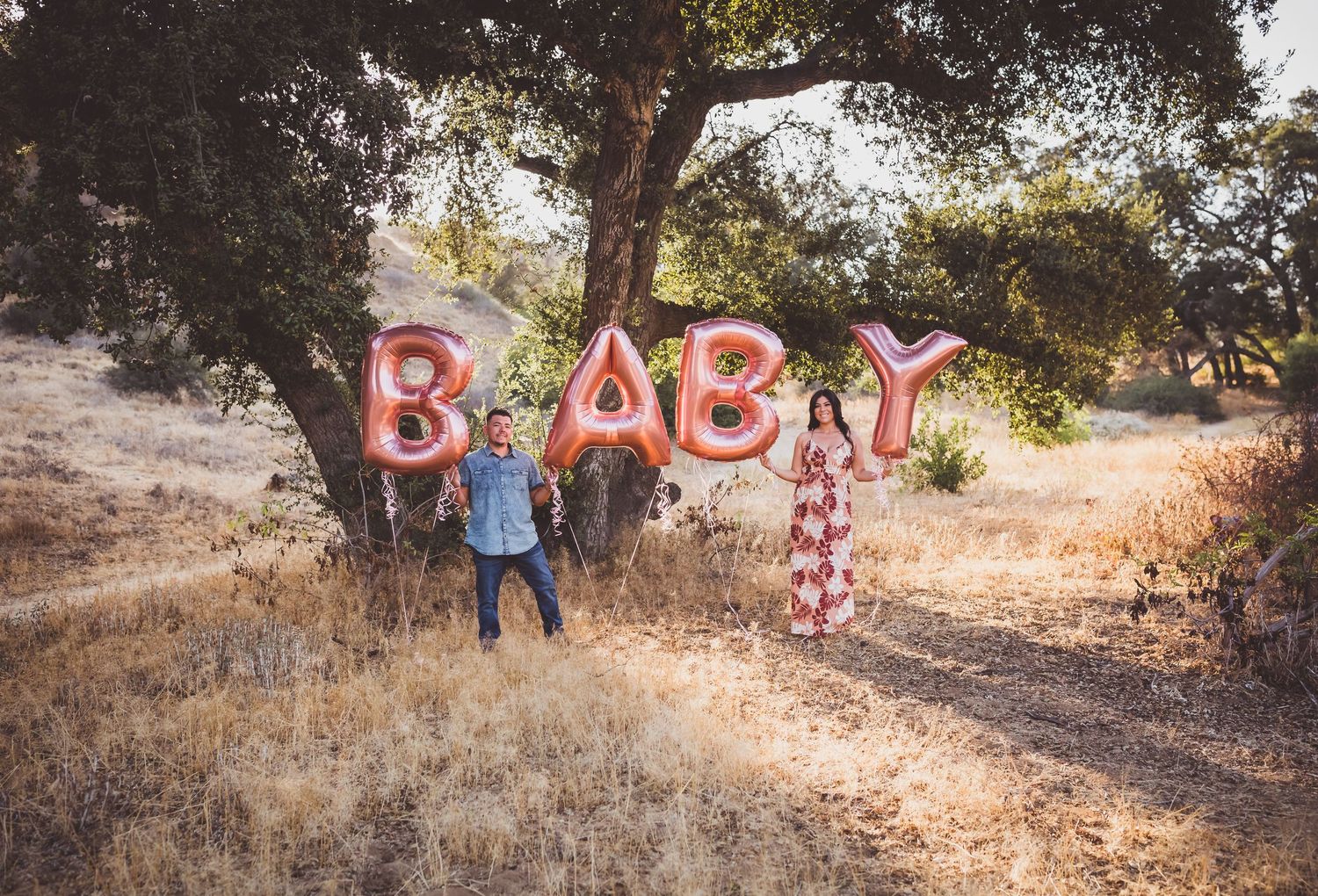 A series of red letter signs spelling 'BABY' arranged along a dirt trail in a rustic outdoor setting during golden hour.