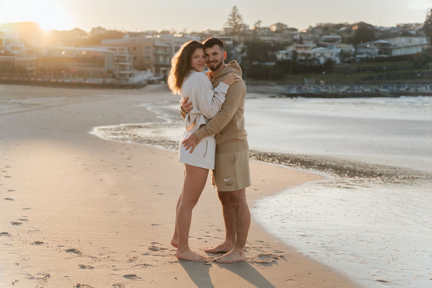 Embracing couple silhouetted against warm sunset light on a sandy Sydney Bondi Beach near the ocean during a Bondi Beach Couple Photoshoot