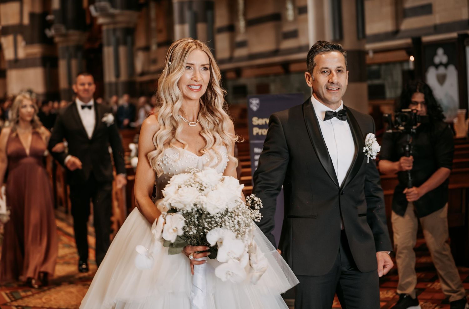 A bride and groom walk together at their wedding celebration while holding hands and smiling.