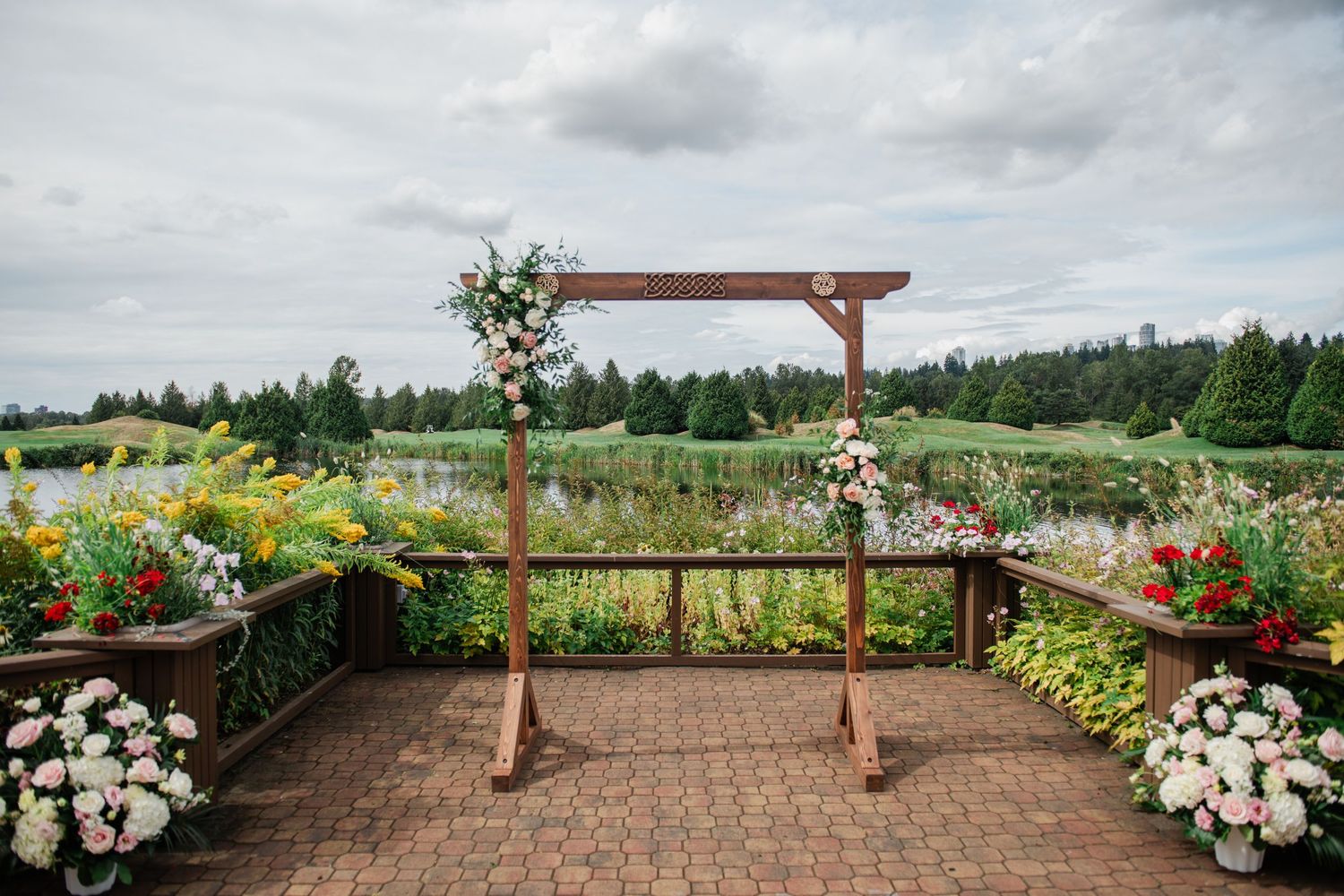 A couple in wedding attire embraces in a field with tall grass and cloudy skies in the background.