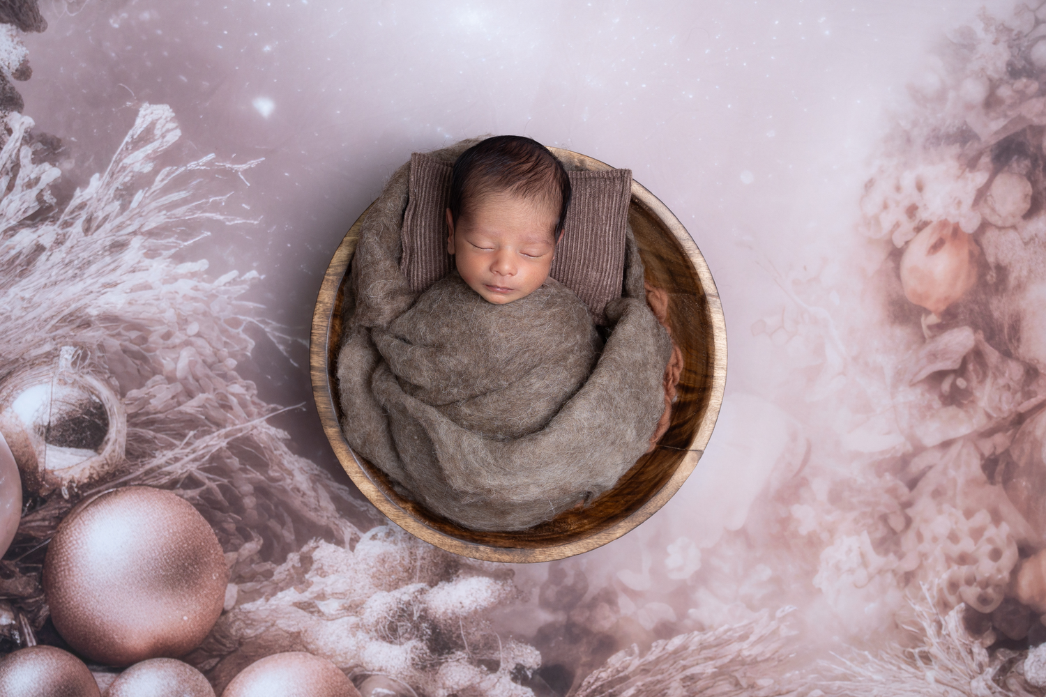 Soft pink and gray newborn photography setup with wraps and props against textured backdrop.