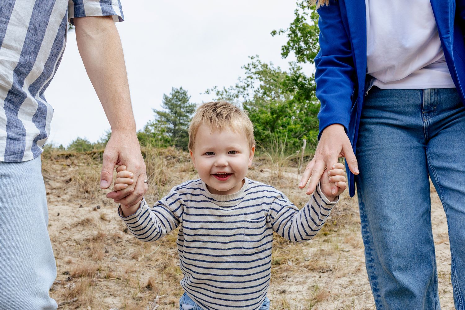 Peuter loopt hand in hand met zijn ouders tijdens een gezinsshoot van Luzan Veenendaal Fotografie in Noord-Holland