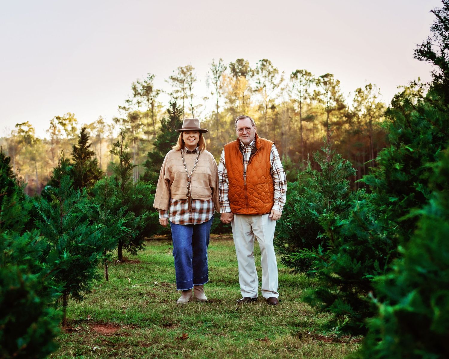 A couple walking in a Christmas Tree farm holding hands